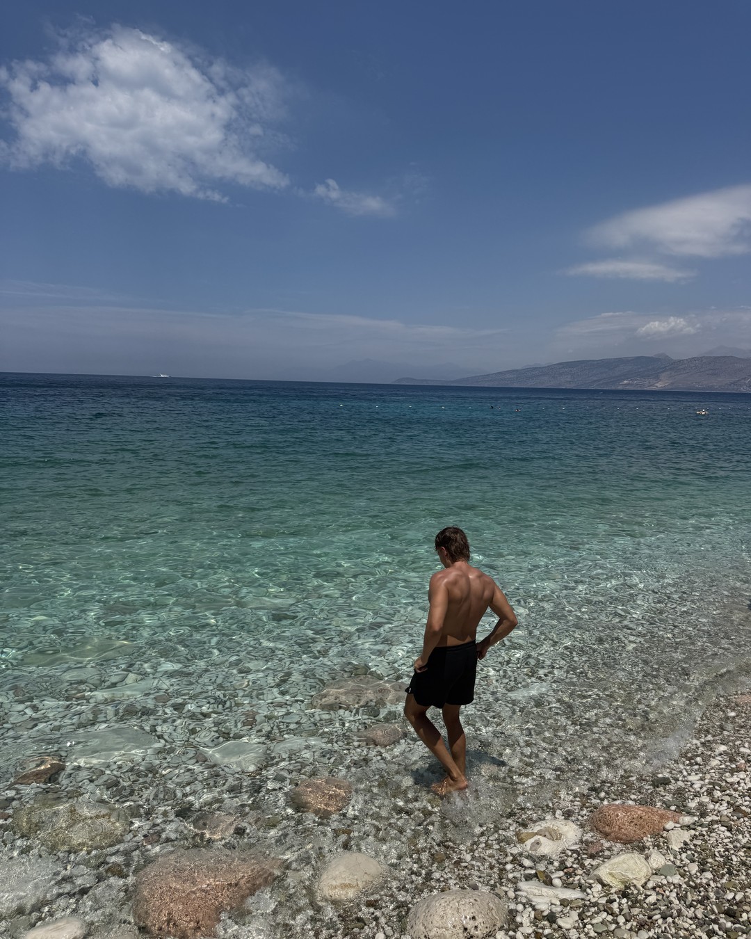 Daniel standing in clear shallow water at Pulëbardha Beach near Sarandë, Albania