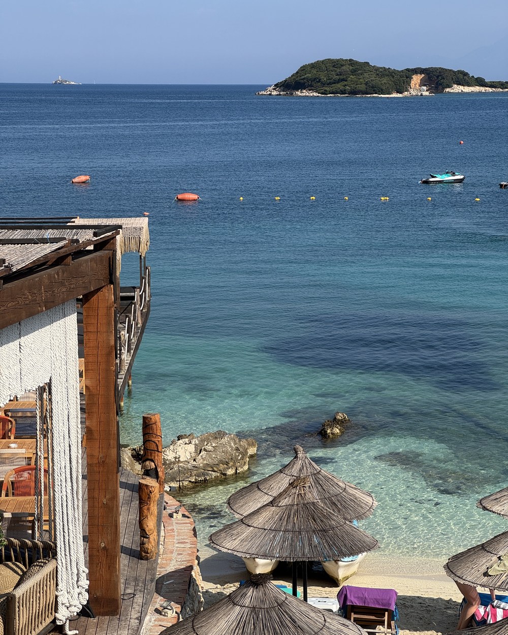 Thatched beach umbrellas above the shoreline with boats out on the bay at Ksamil, Albania