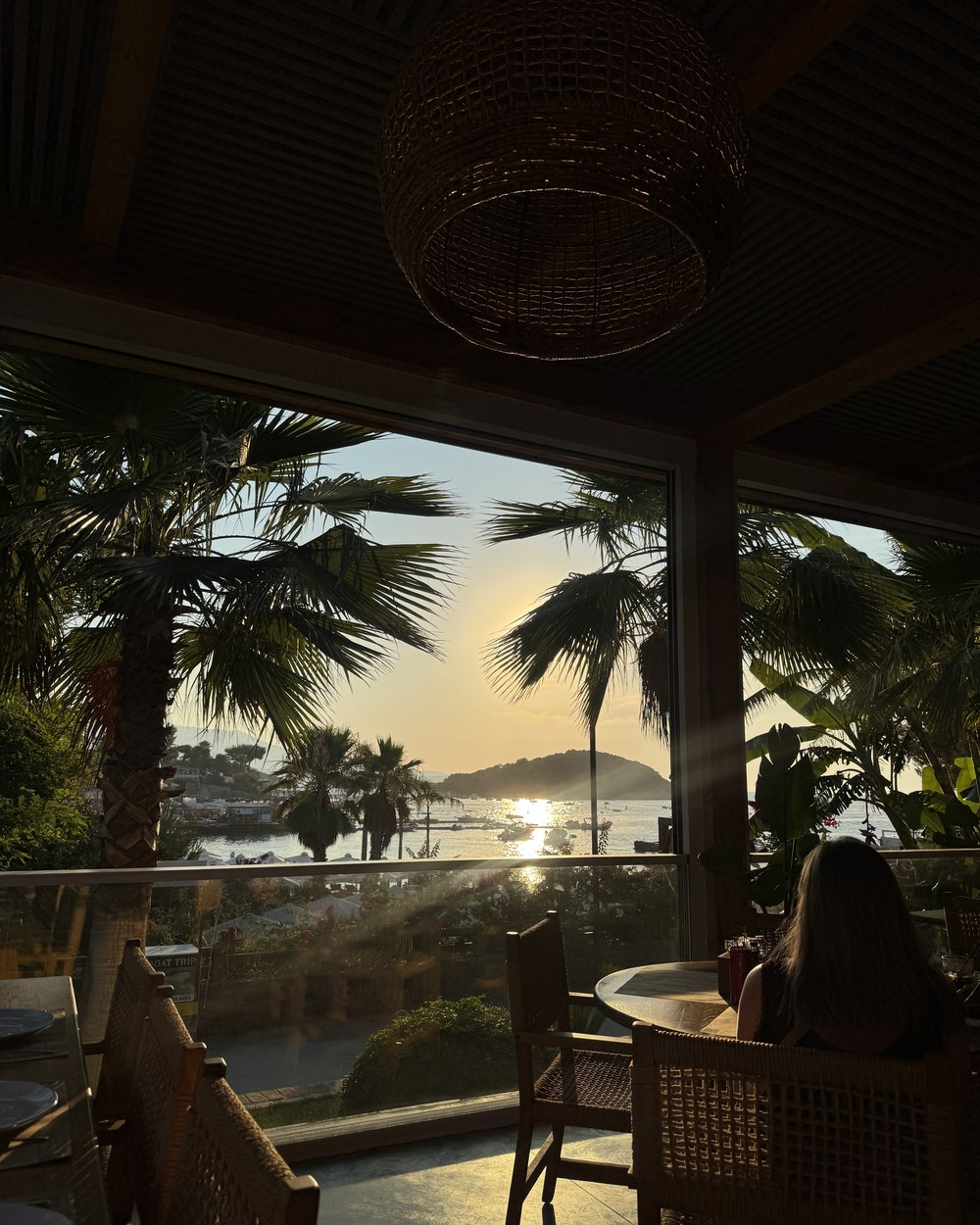 Sunset over the water framed by palm trees from a restaurant terrace in Ksamil, Albania