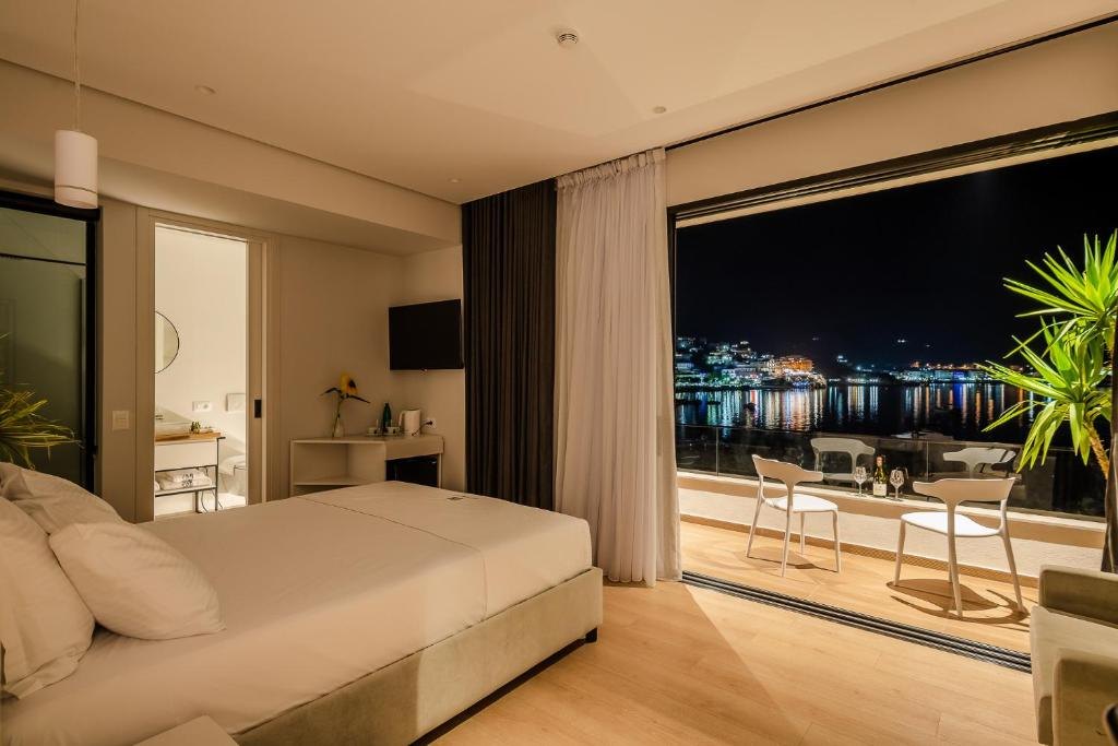 Hotel room with a bed facing open glass doors onto a balcony above the lit bay at Rea Boutique Hotel in Himarë