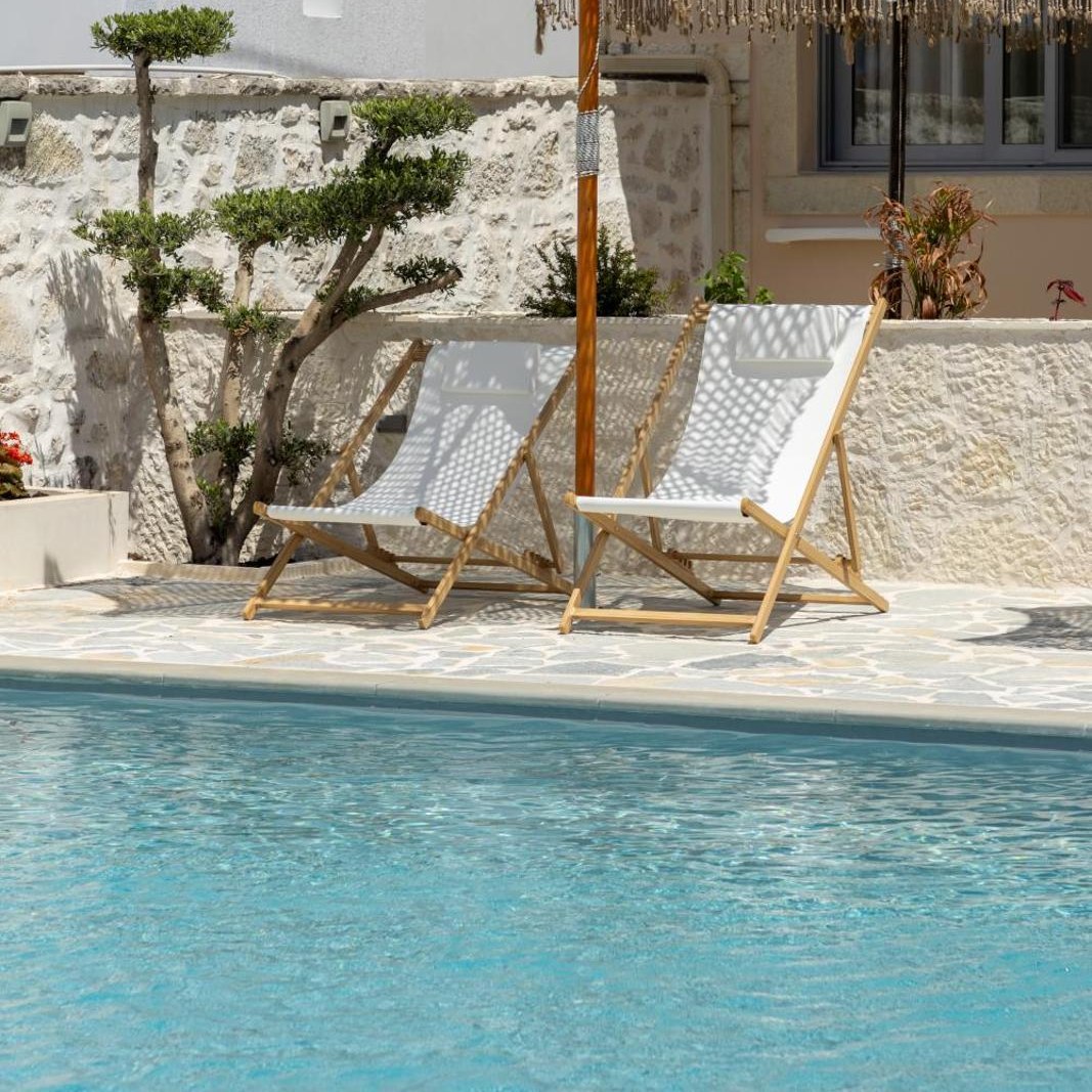 Two deck chairs and a fringed parasol on the terrace beside the pool at Dimitri Hotel in Himarë