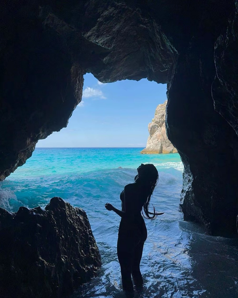 Ellen silhouetted in the mouth of Pirate Cave above bright turquoise water near Himarë, Albania