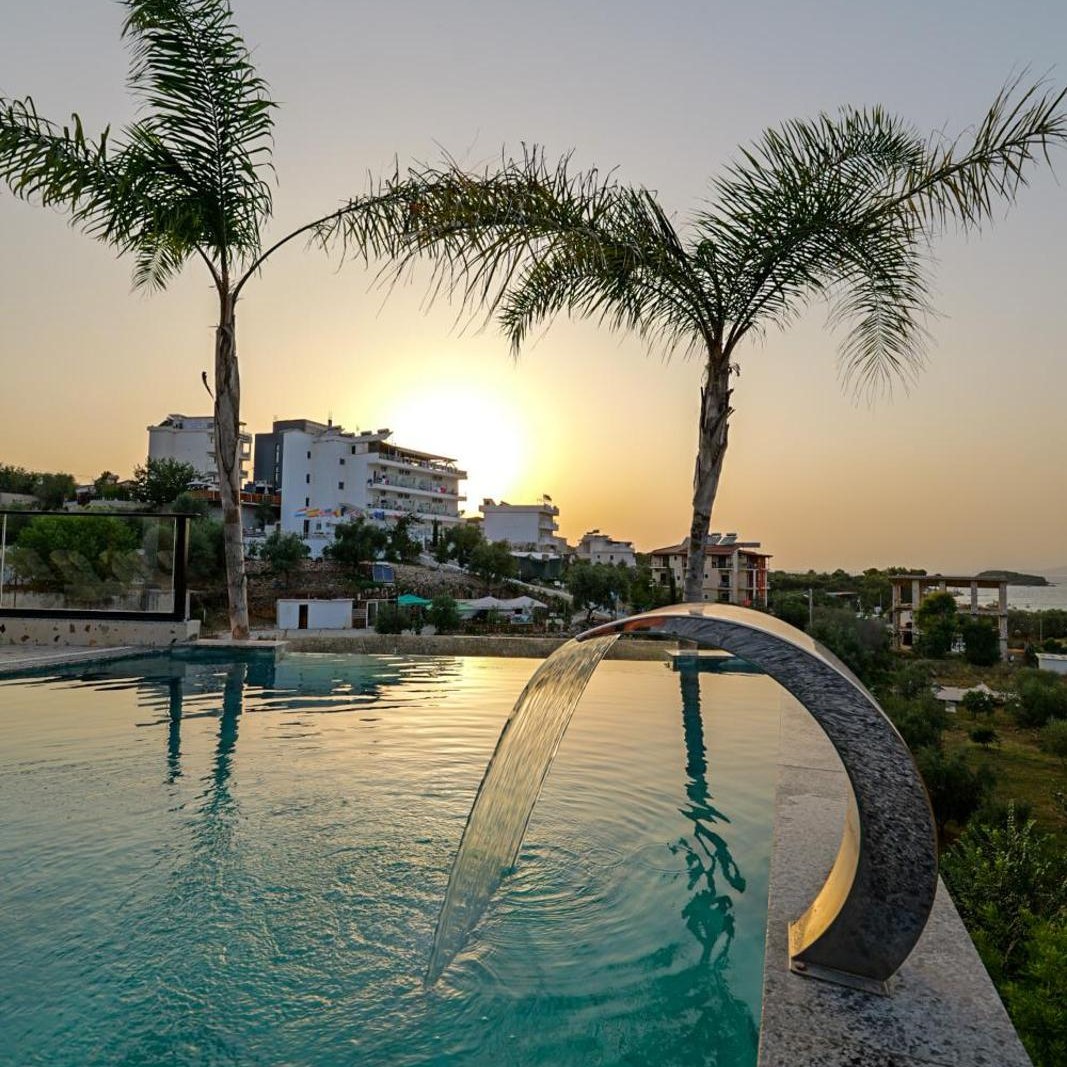 Swimming pool lined with palm trees at sunset at Sunlight Hotel in Ksamil, Albania