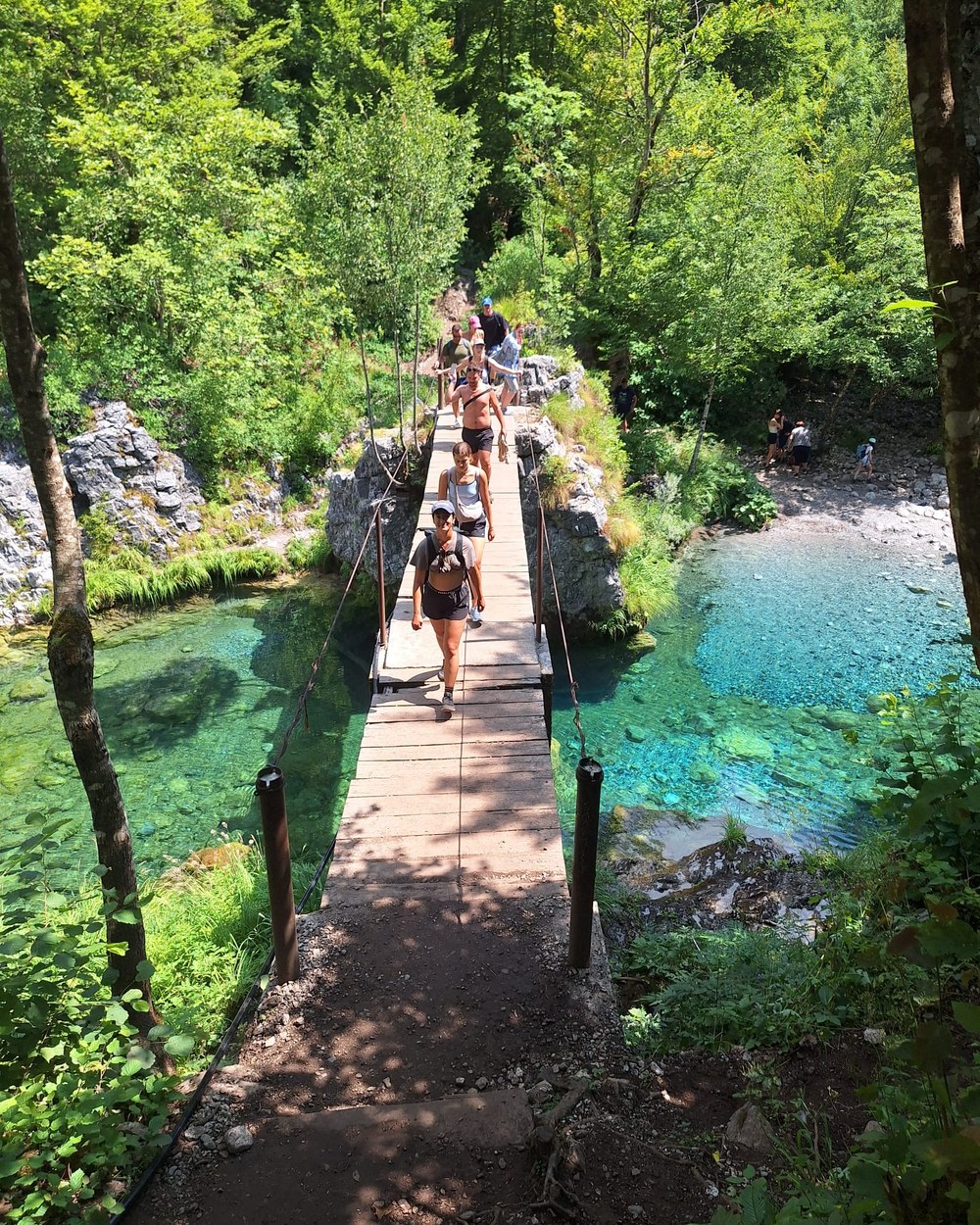 Walkers crossing a wooden boardwalk beside the river on the trail to the Theth Blue Eye