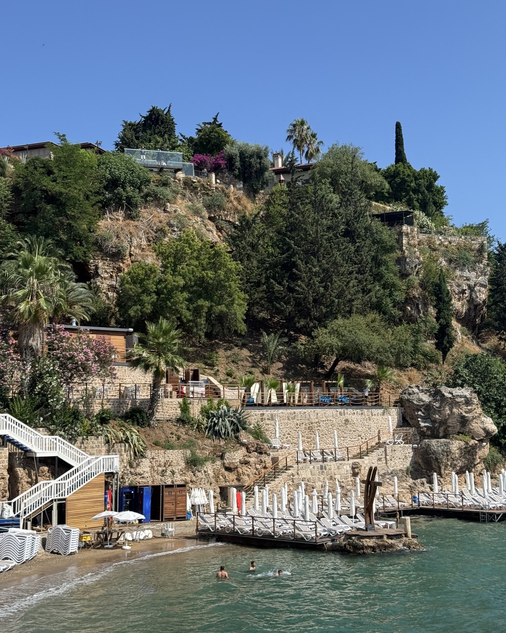 Cliffs above a small beach club and swimming platform in Antalya with pine trees above