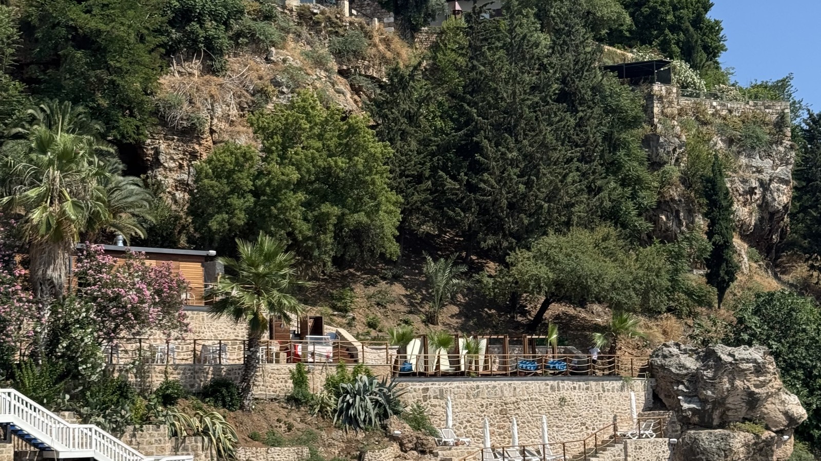 Cliffs above a small beach club and swimming platform in Antalya with pine trees above