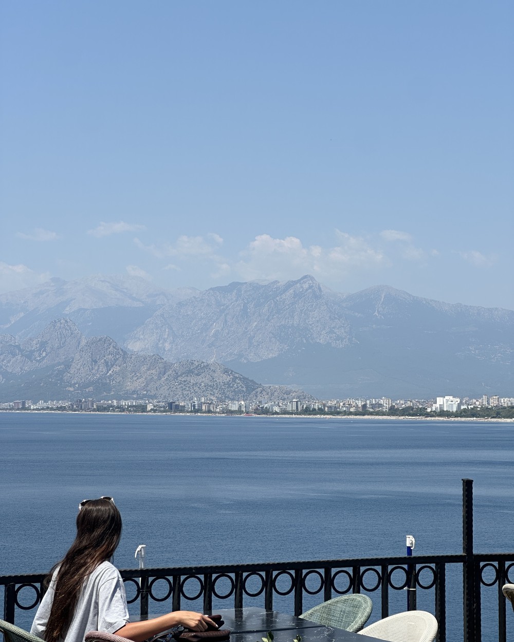 Woman sitting at a table on a terrace looking out over the bay and mountains in Antalya