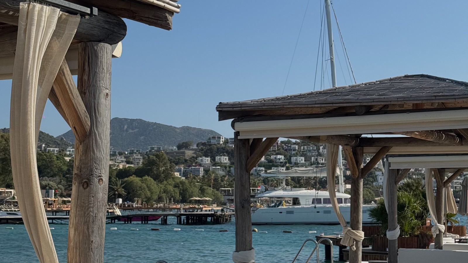 Cabana with white curtains on a wooden deck over the sea at Villa Azur beach club in Bodrum