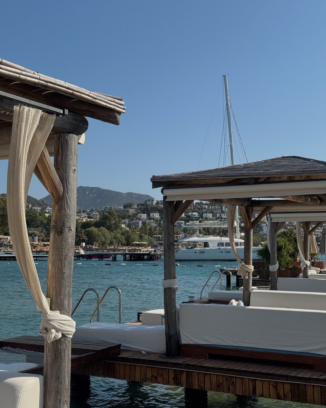 Cabana with white curtains on a wooden deck over the sea at Villa Azur beach club in Bodrum