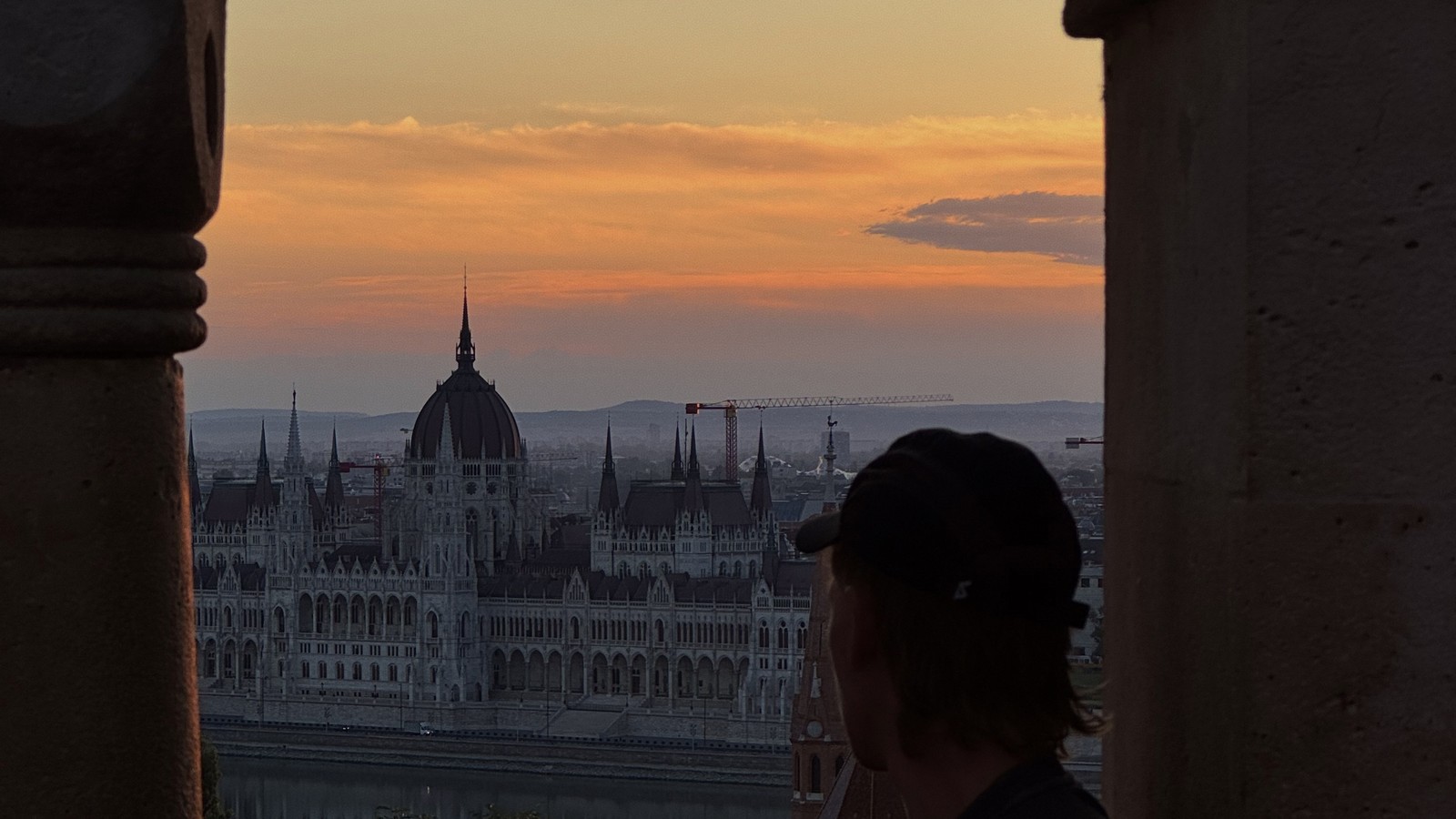 Man looking out through a stone arch at Fisherman's Bastion towards the Hungarian Parliament