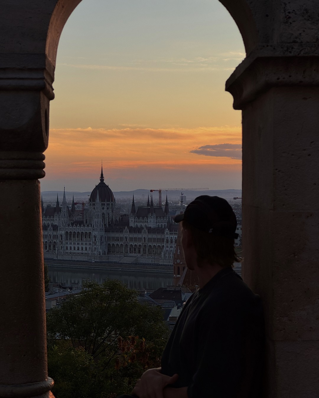 Man looking out through a stone arch at Fisherman's Bastion towards Parliament