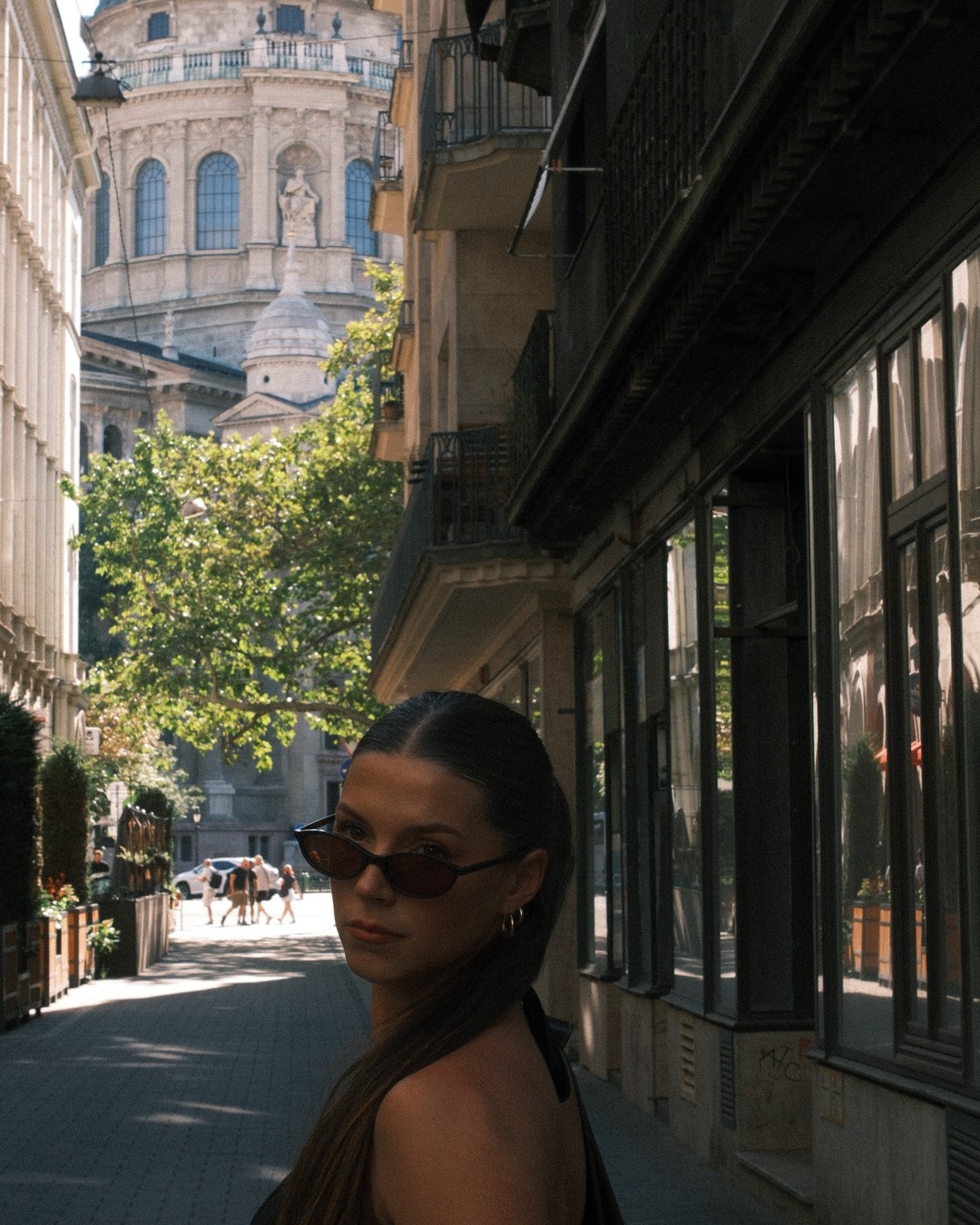 Woman in sunglasses on a sunlit Budapest street with St Stephen's Basilica behind
