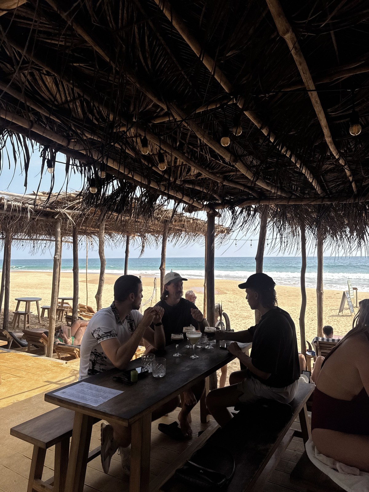 Friends seated at a table under the thatched roof of Amaroo café, facing Hikkaduwa beach