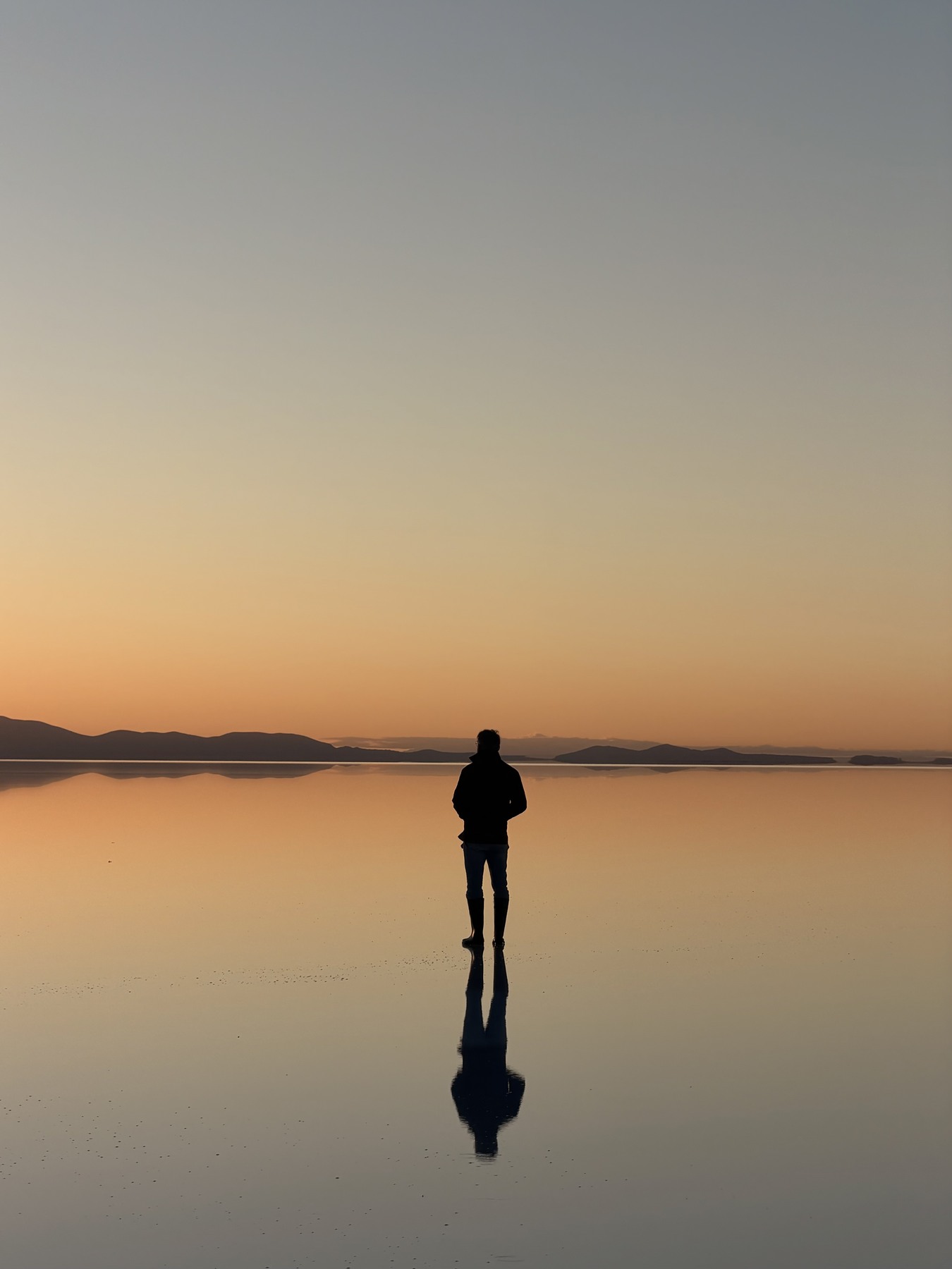 A traveller reflected in golden sunrise light on the Uyuni salt flats