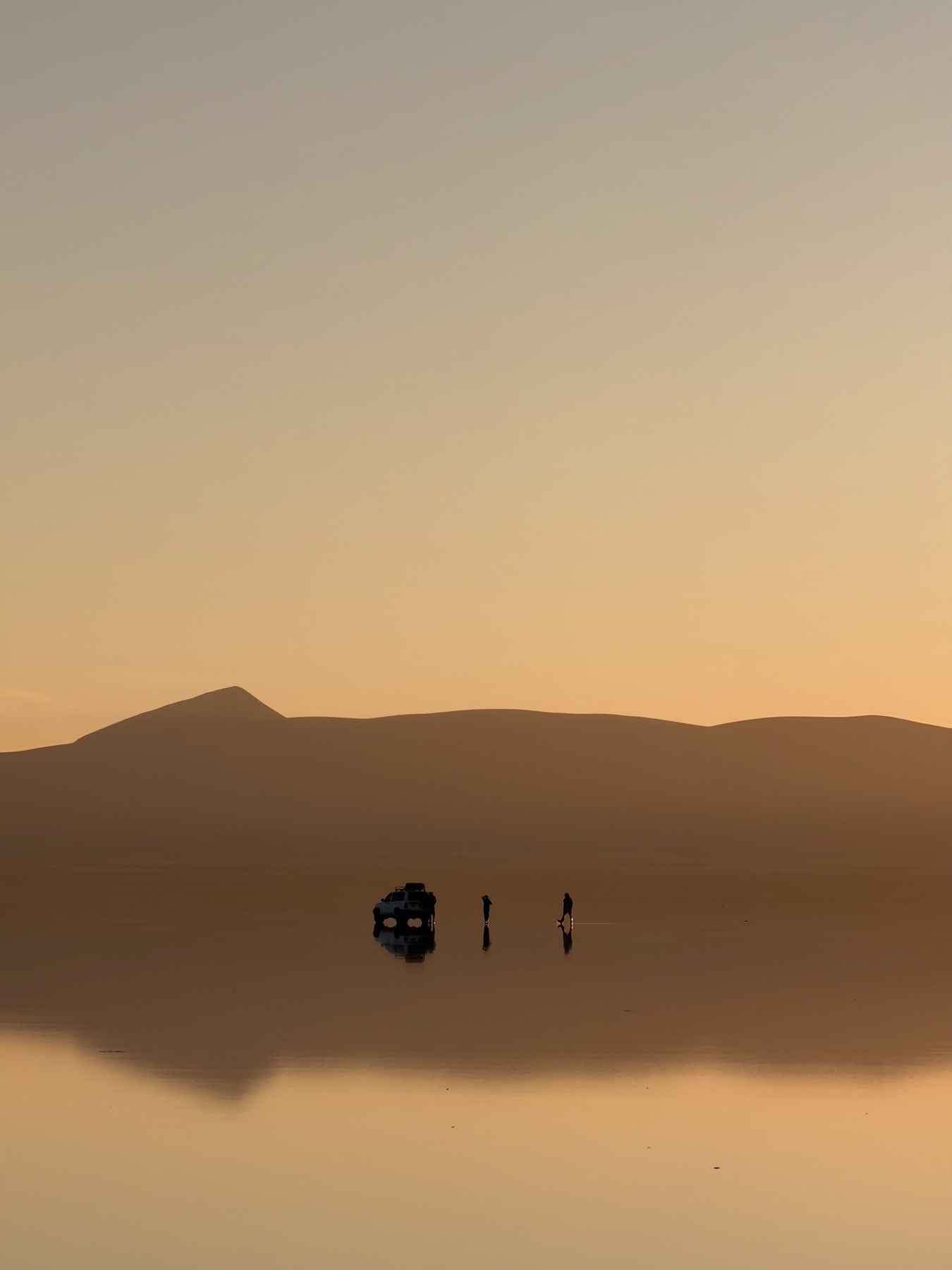 Golden mountains and a distant vehicle reflected on the Uyuni salt flats