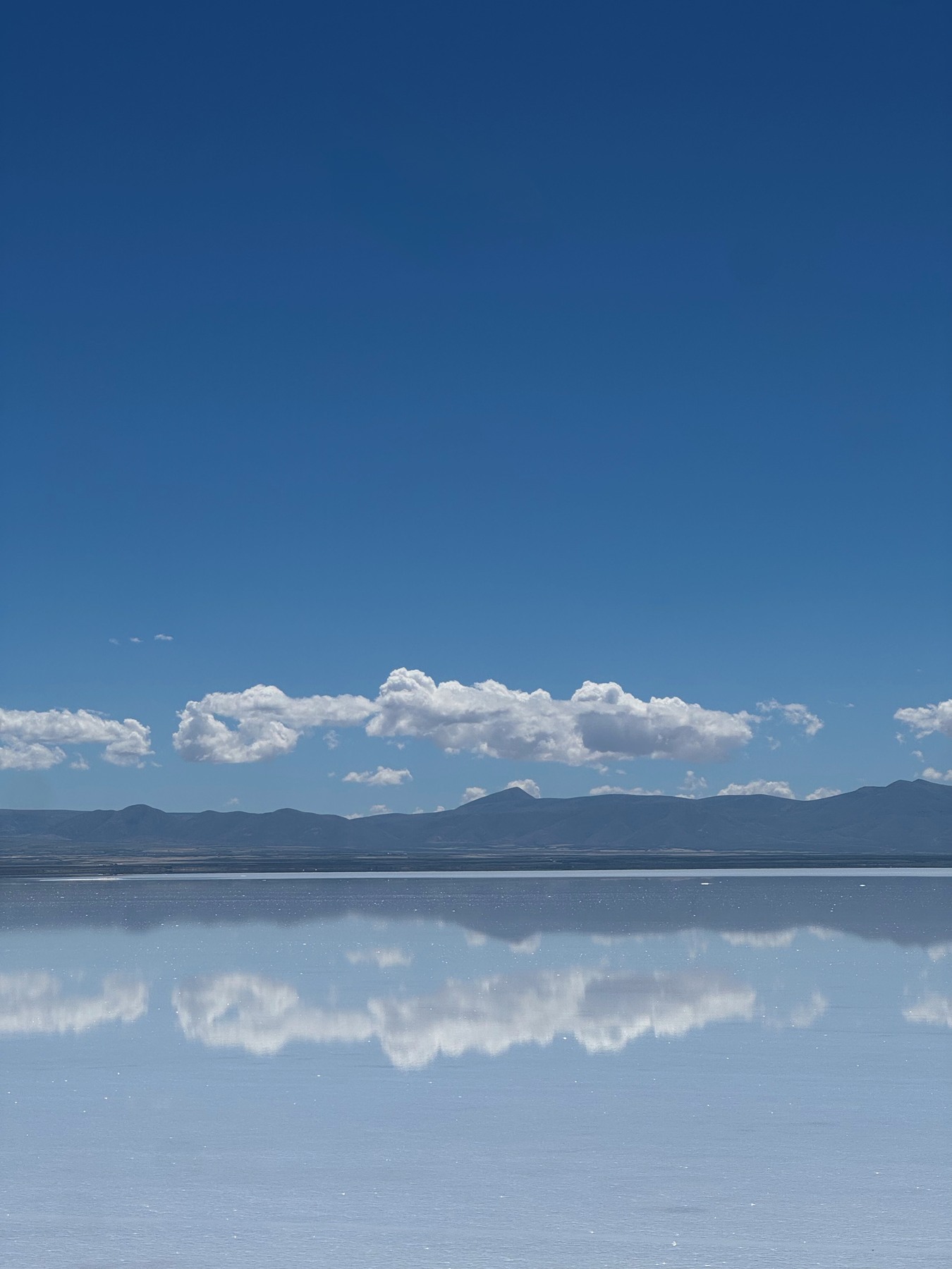 White clouds and distant mountains reflected in the Uyuni salt flats