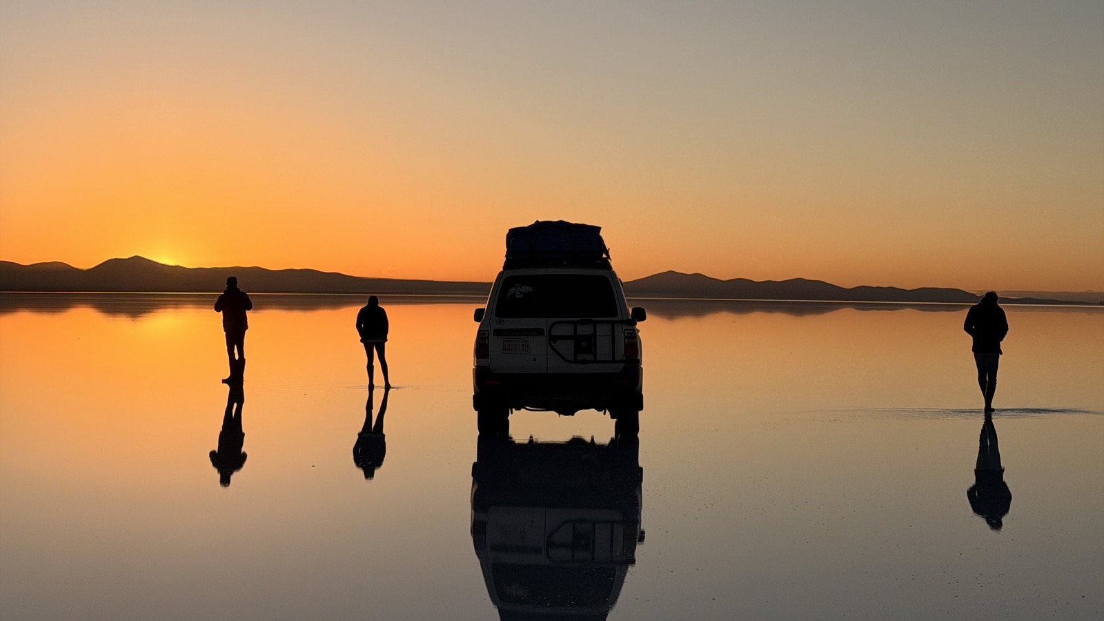Our group and four-wheel drive reflected on the Uyuni salt flats at sunrise