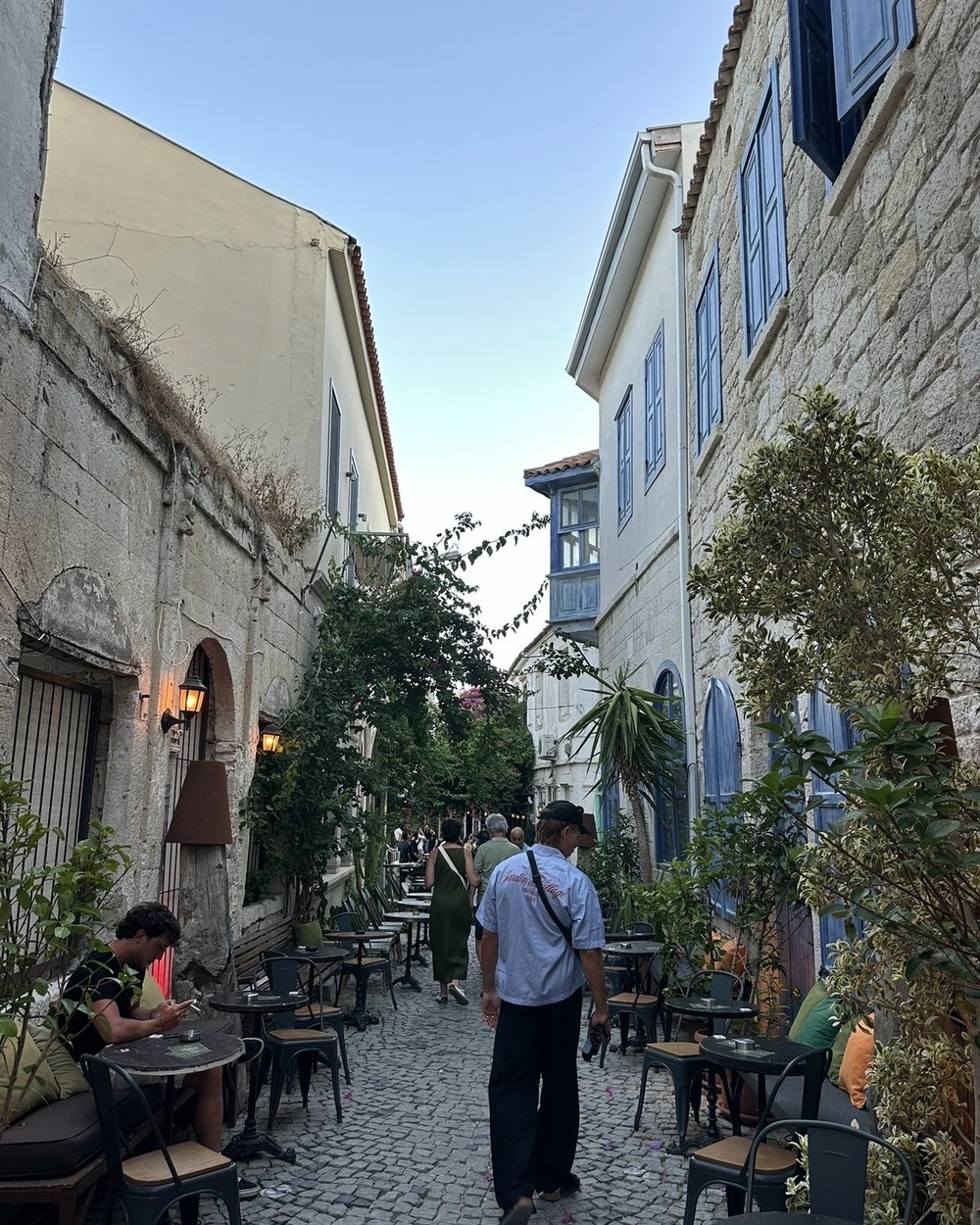 Cobbled street lined with restaurants and bougainvillea in Alaçatı, Türkiye