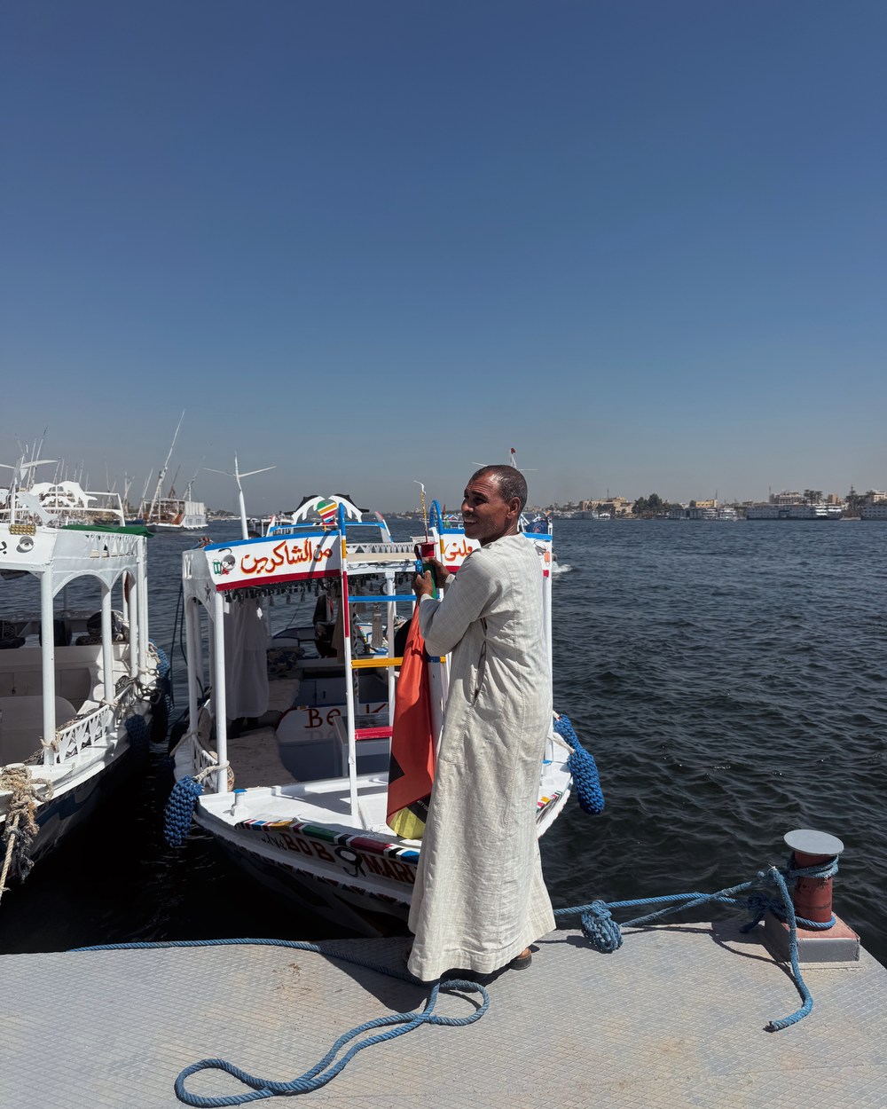 A local boat captain beside the colourful passenger boats used to cross the Nile in Luxor