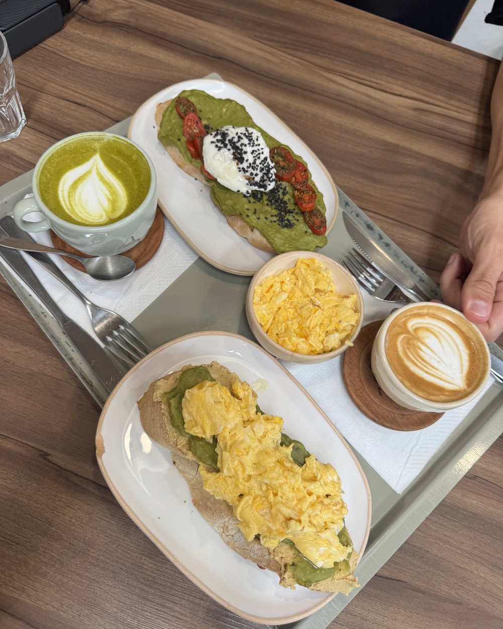 Avocado toast with a poached egg, avocado toast with scrambled eggs, a green latte and a cappuccino on a tray at Calafate Coffee Roasters