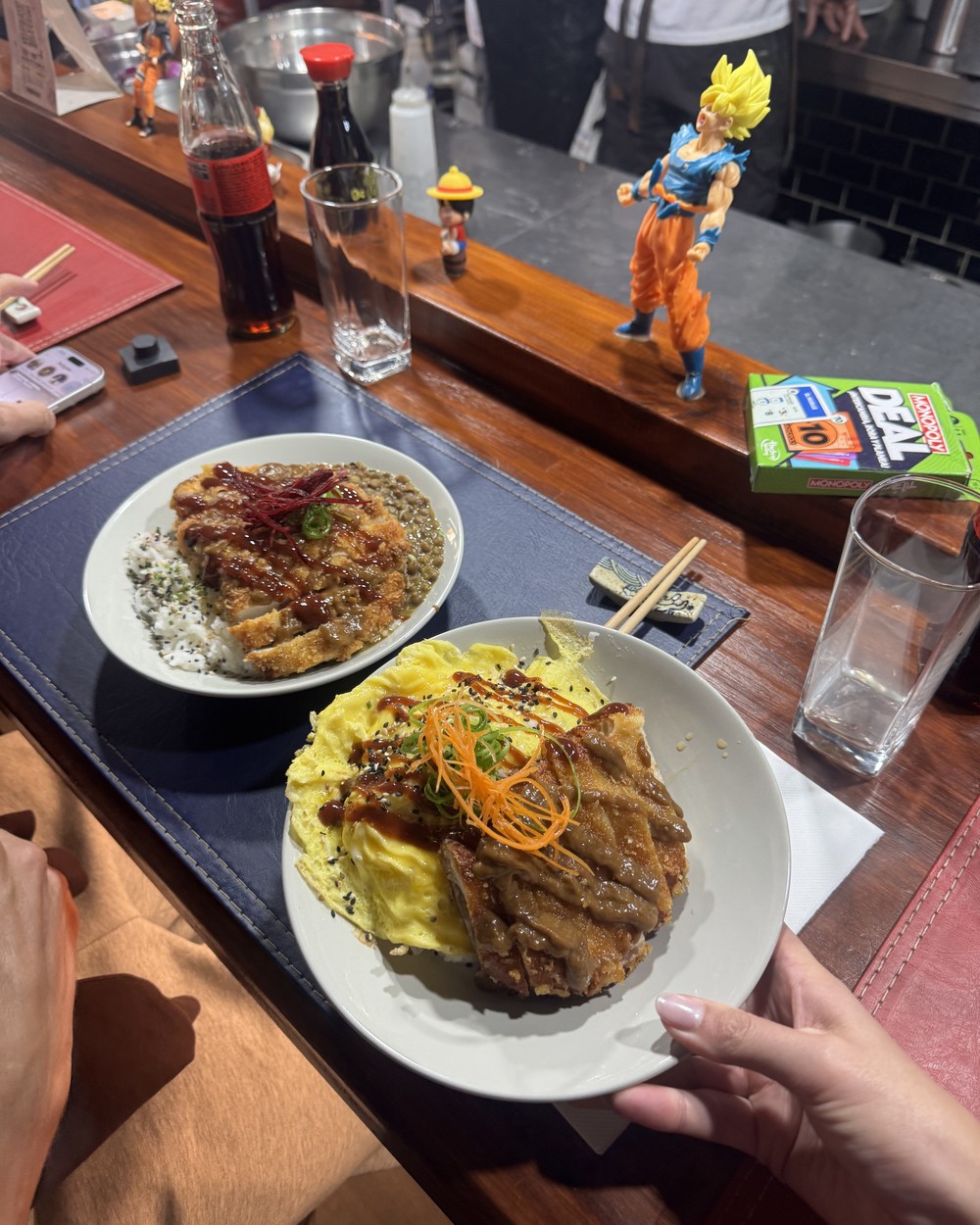 Chicken curry with lentils and a don with omelette at the counter of Maki Go, with anime figures behind