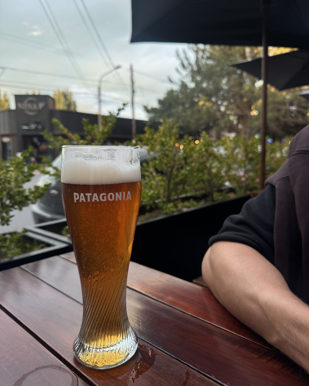 A Patagonia beer in a tall branded glass on an outdoor table in El Calafate, with Daniel's arm beside it