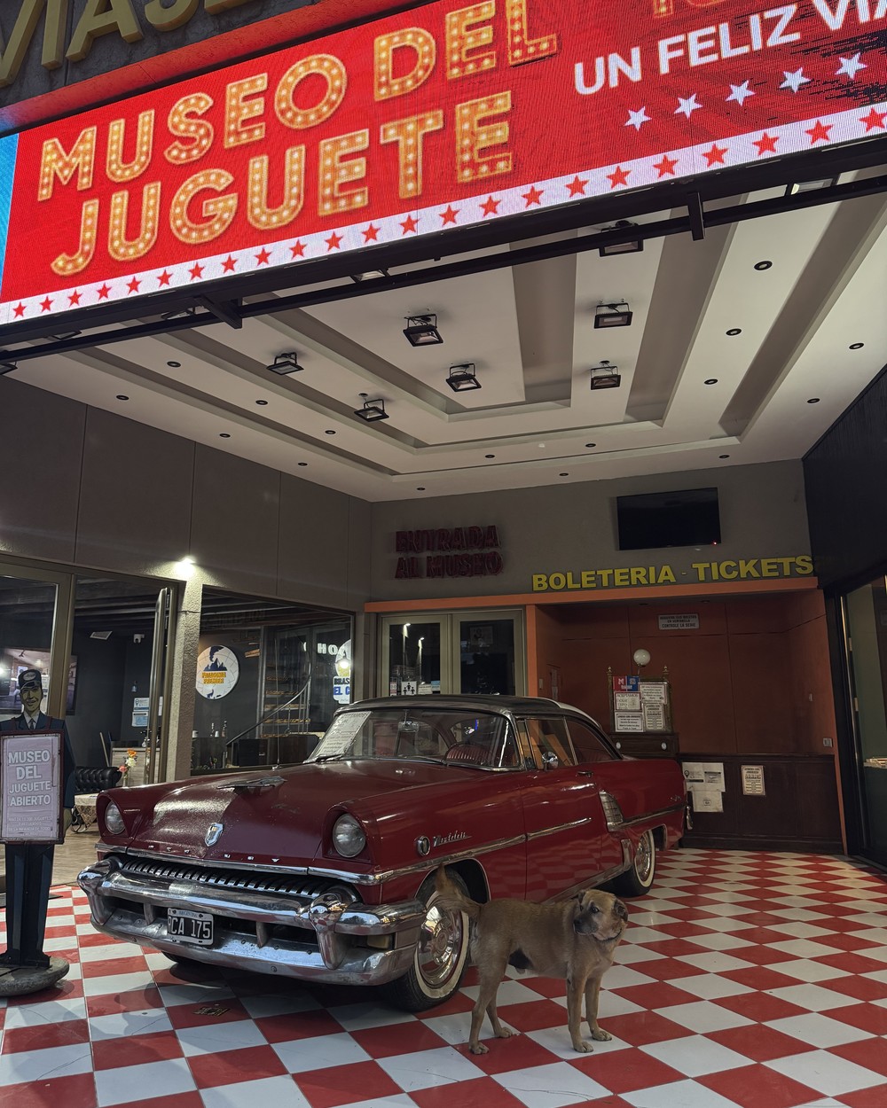 A vintage red car and a dog at the entrance of the Museo del Juguete in central El Calafate