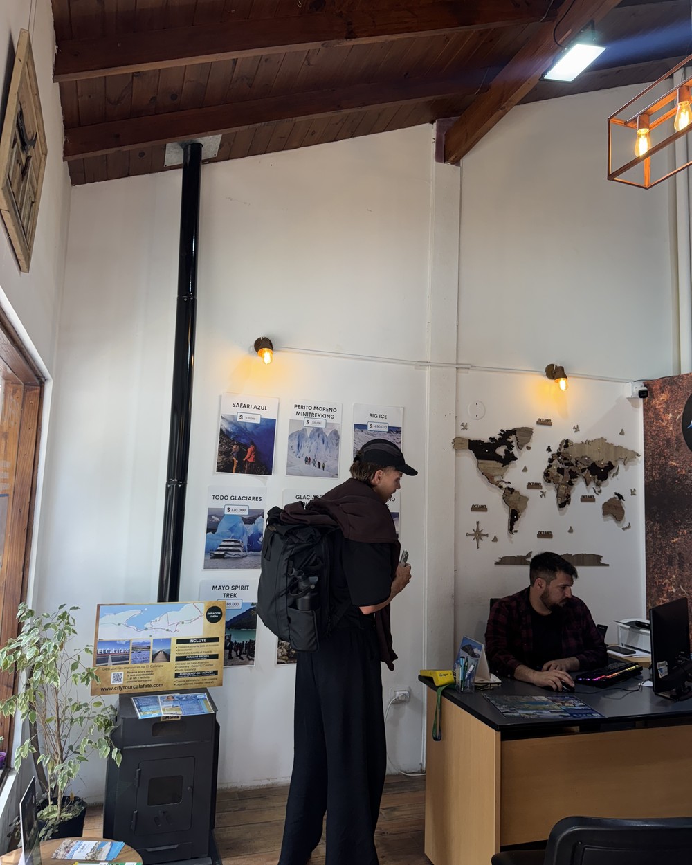 Daniel at the desk of the tour office in El Calafate where we booked our private driver, with glacier tour posters on the wall
