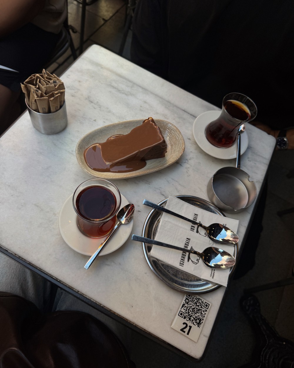 A slice of Basque cheesecake with caramel sauce on a plate beside Turkish tea in Istanbul