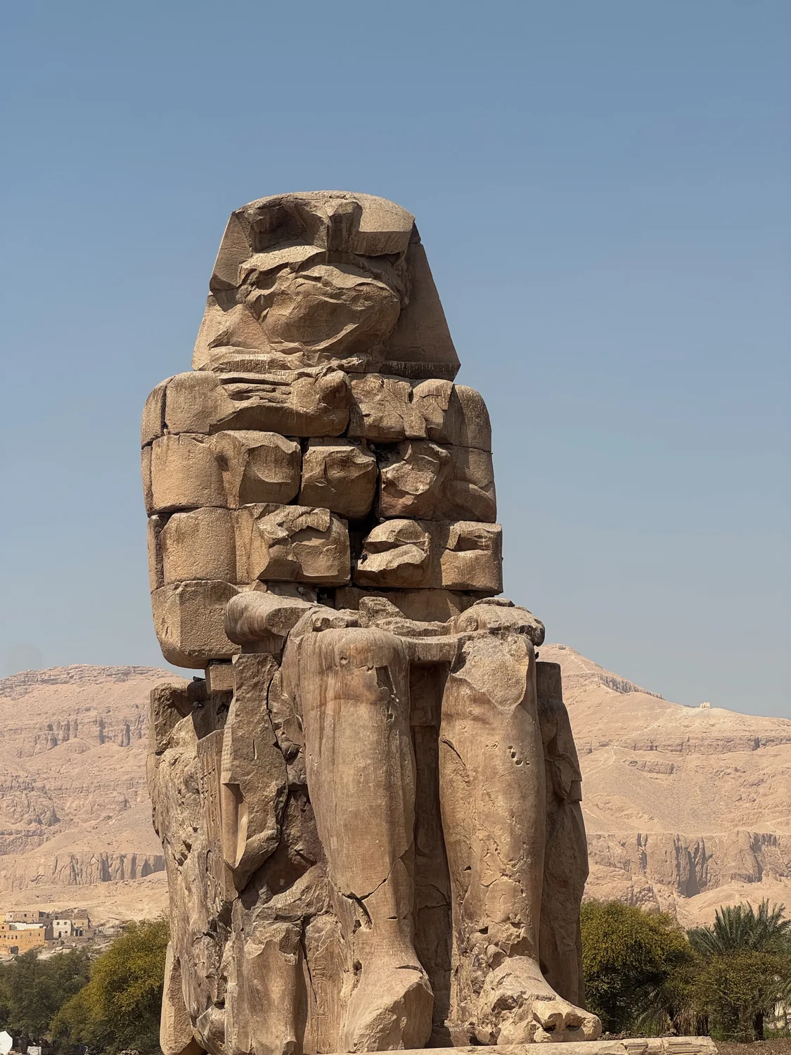 One of the Colossi of Memnon statues with the West Bank hills behind it in Luxor