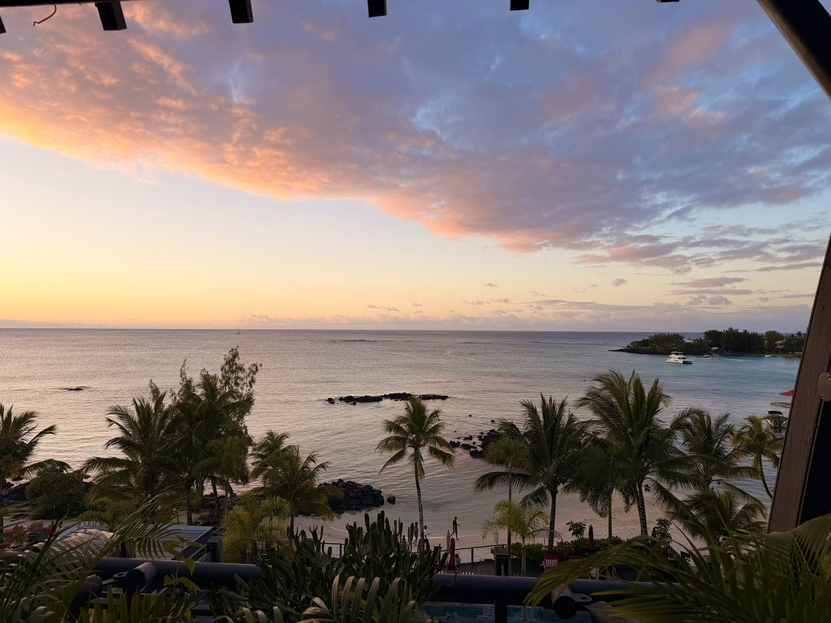 Pink and gold sunset over a Mauritius bay with palms and small boats below