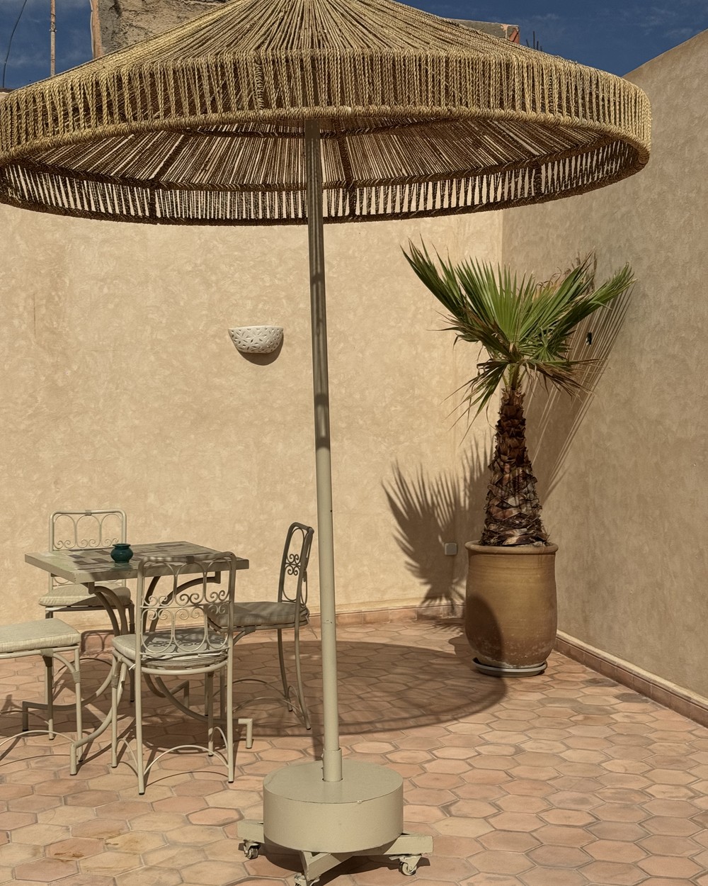 Shaded rooftop table under a woven parasol at a riad in Marrakech, Morocco
