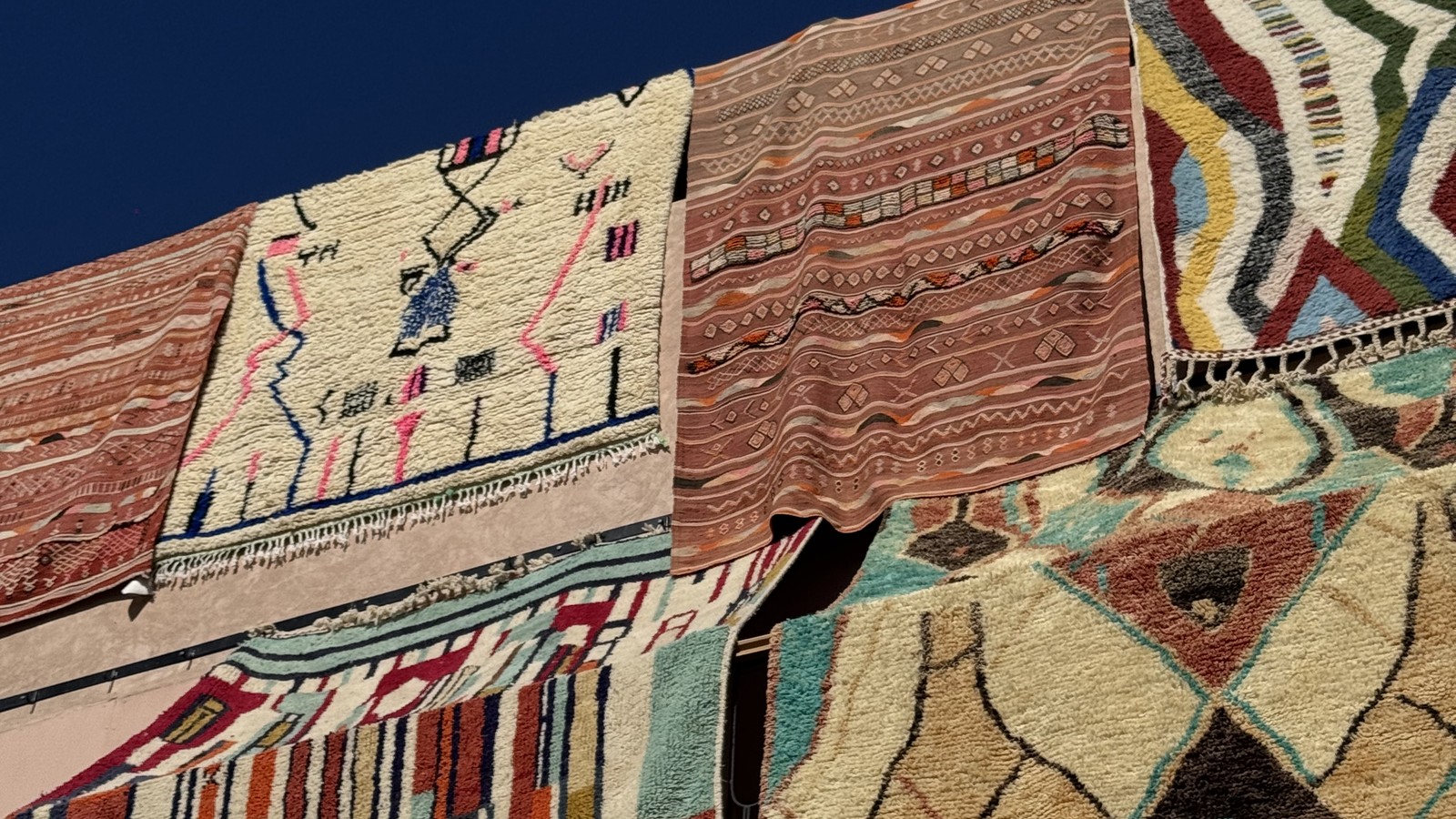 Handwoven Berber rugs hanging on a wall against a deep blue sky in Marrakech, Morocco