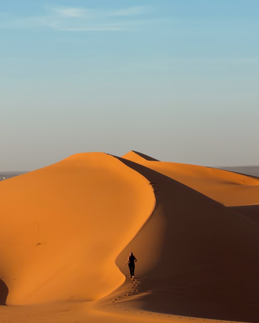 A huge curving sand dune rising above the flat desert at Merzouga in the Sahara, Morocco