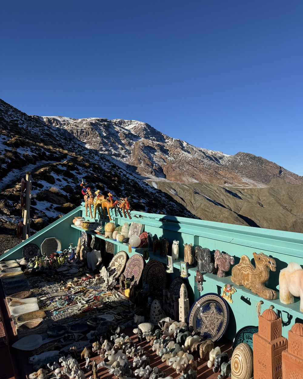 Snow on the High Atlas peaks above a roadside stall selling fossils and minerals at the Tizi n Tichka pass, Morocco