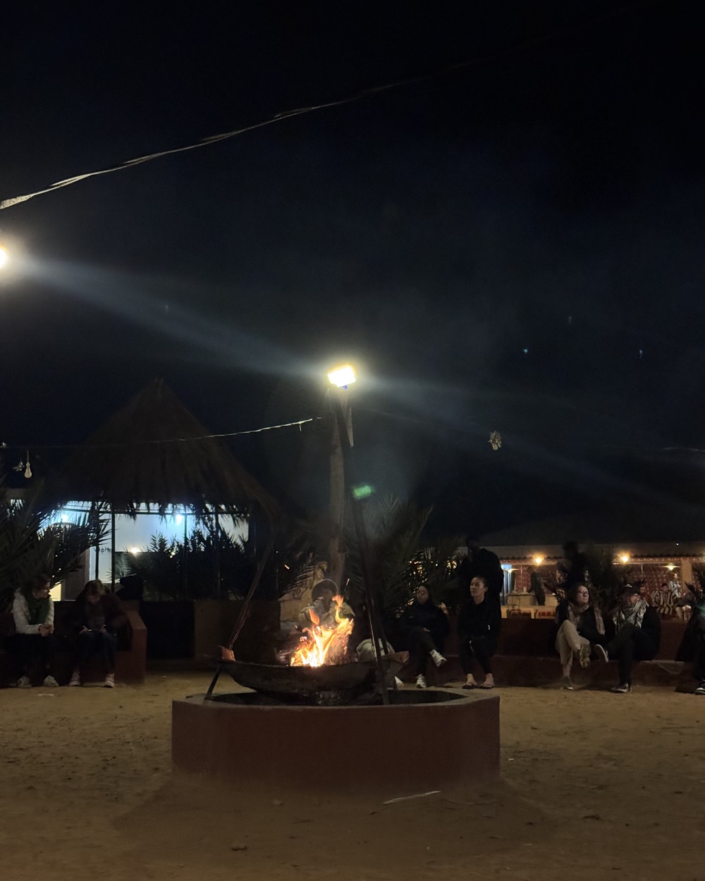 Group gathered around a fire pit at a Sahara desert camp after dark near Merzouga, Morocco