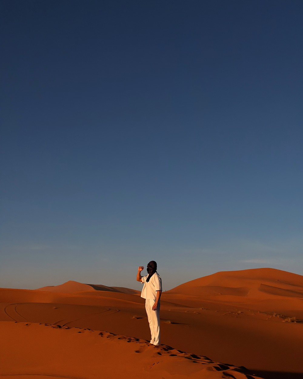 Standing on the crest of a tall sand dune under a deep blue sky in the Sahara near Merzouga, Morocco