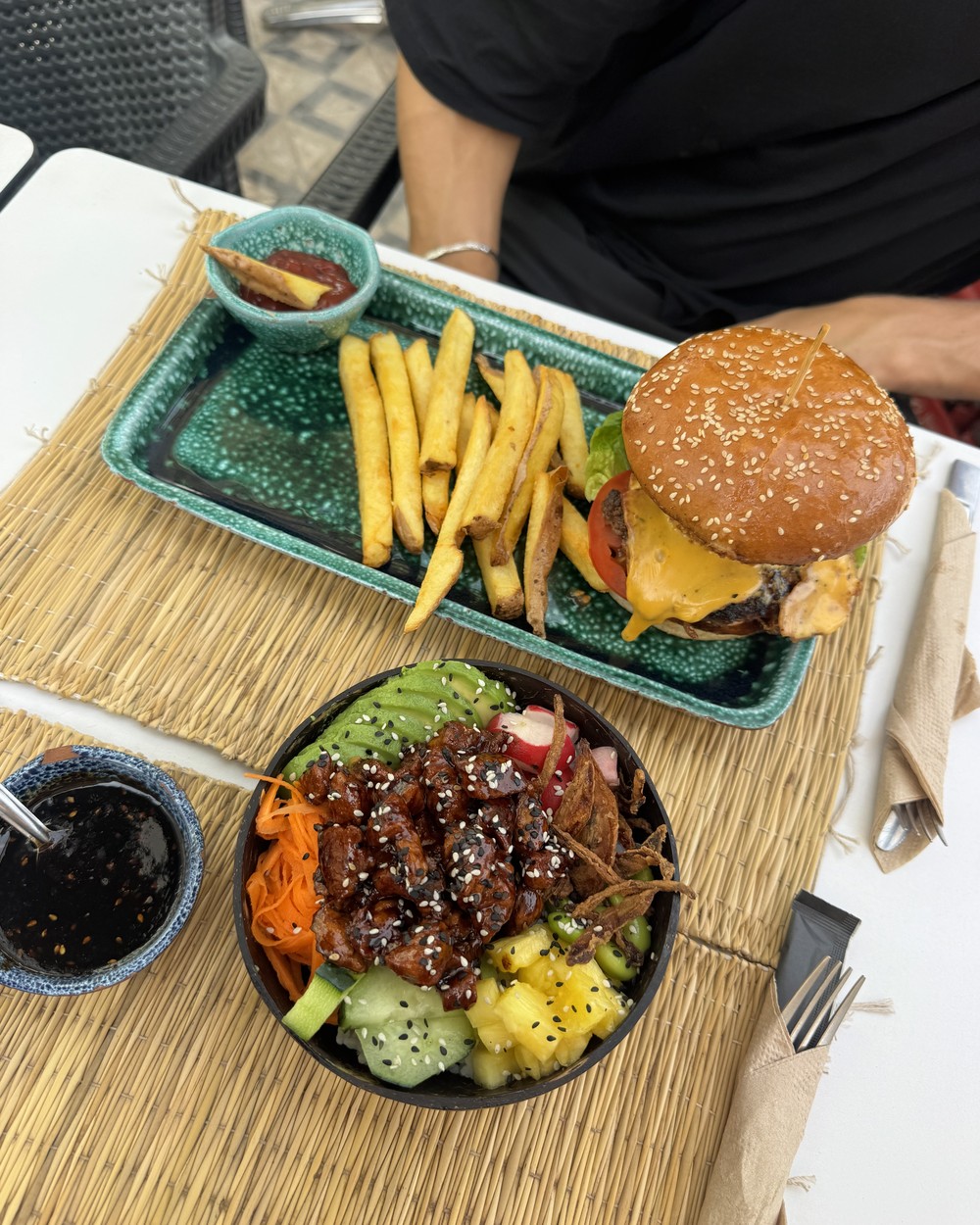 Burger with fries and a poke bowl on a woven table at Ohana Poke and Vitamin Bar in Tamraght, Morocco