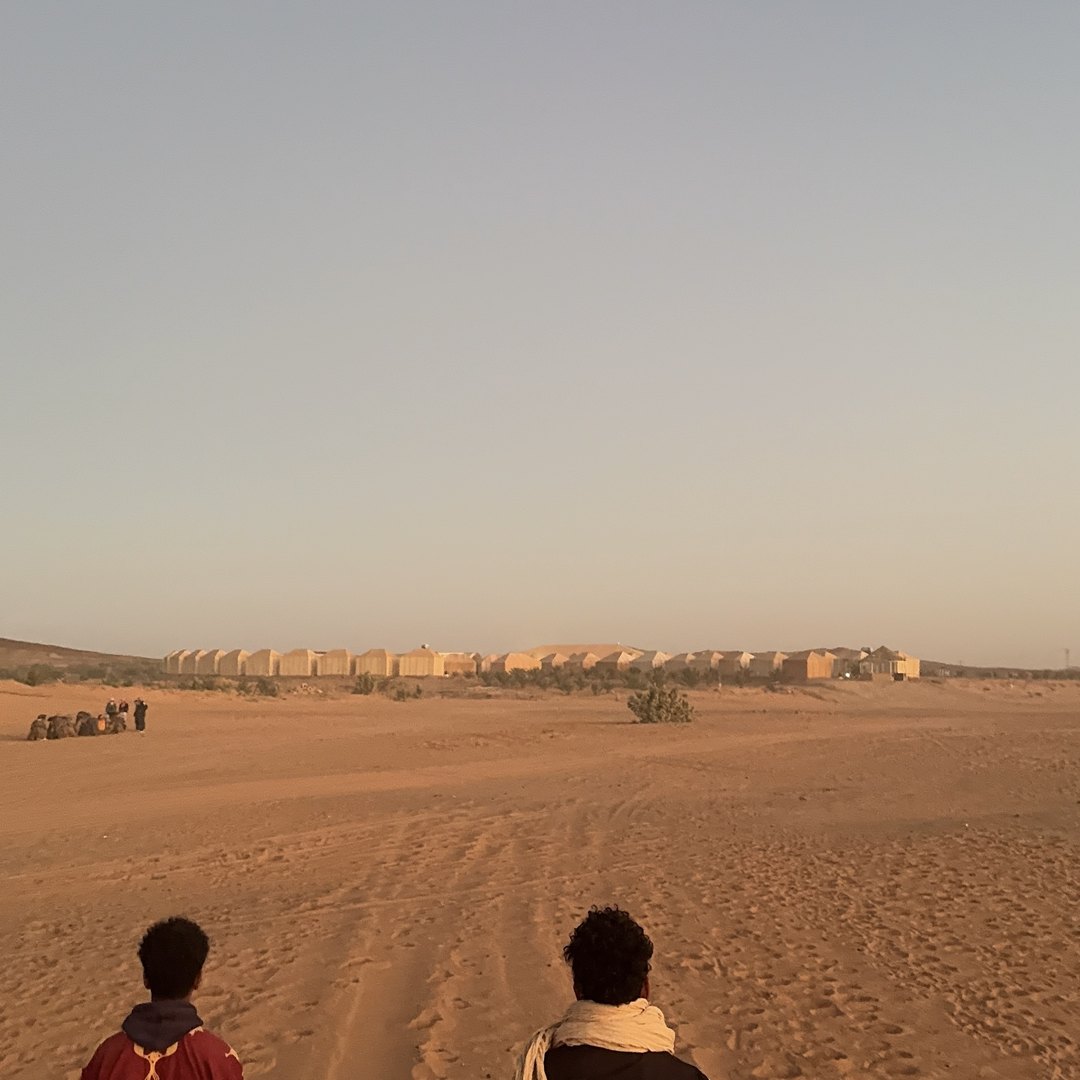Two people walking across the sand towards the desert camp at Merzouga in the Sahara, Morocco