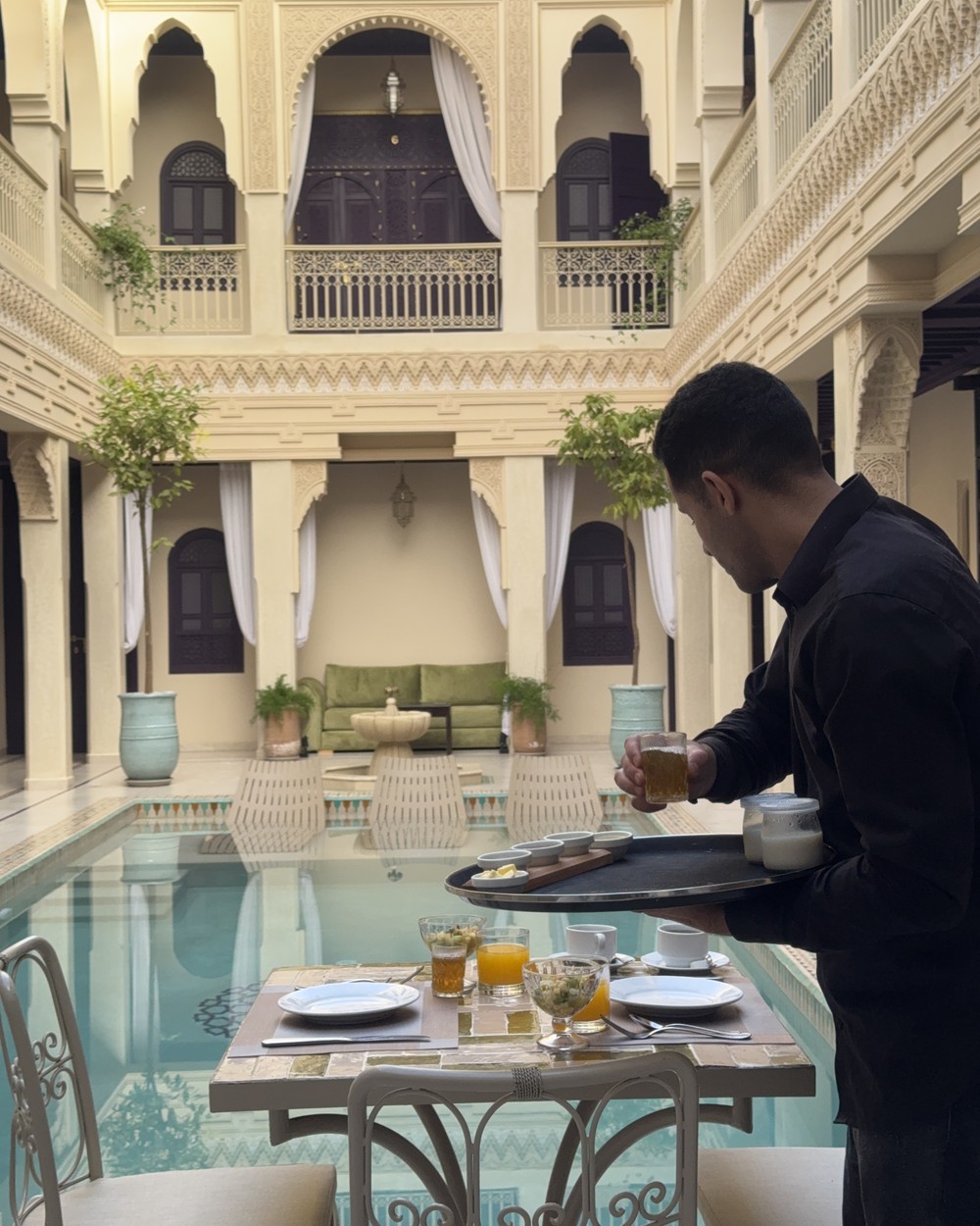 Waiter carrying a tray of mint tea beside the courtyard pool of a riad in Marrakech, Morocco