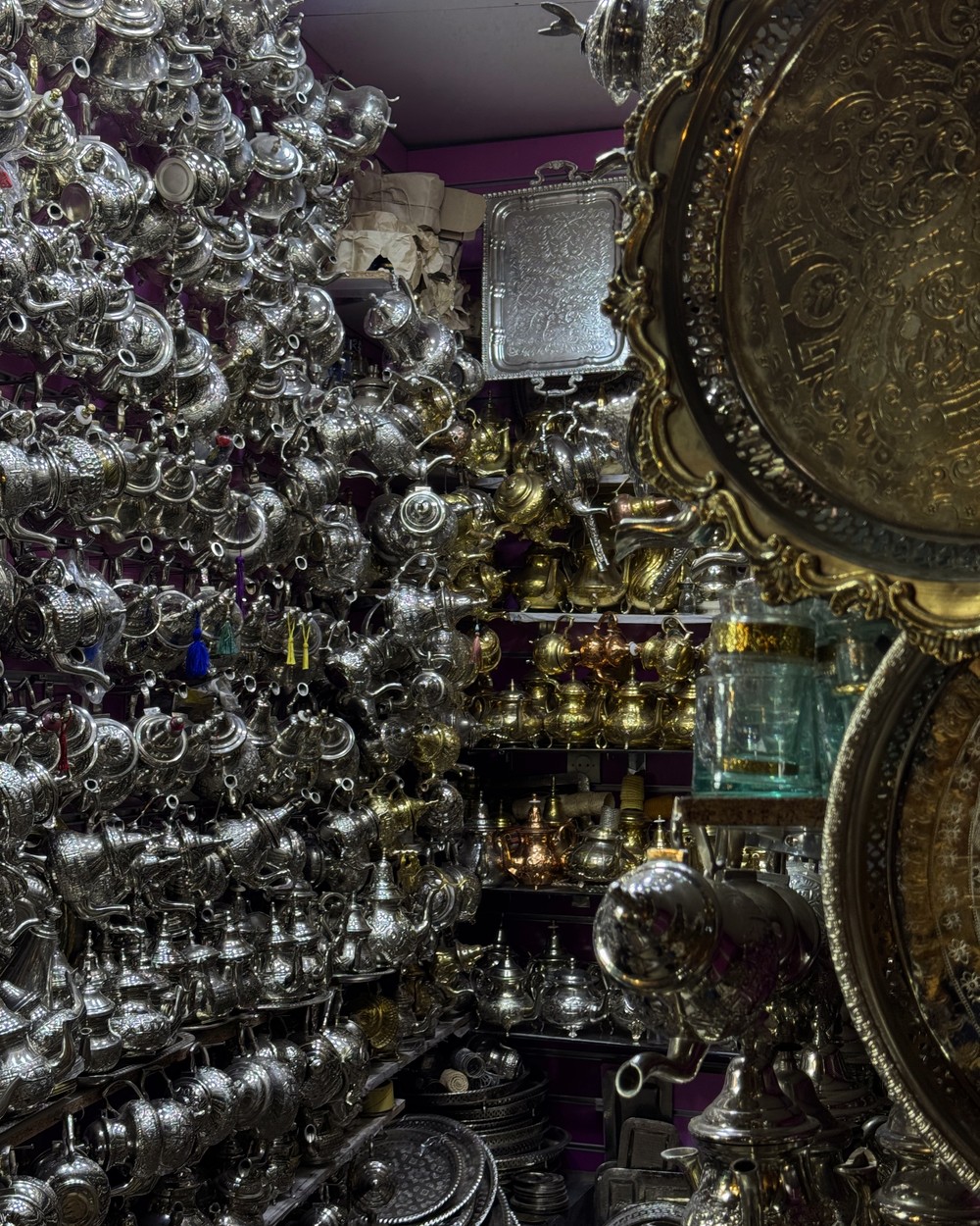 Silver teapots and engraved brass trays stacked in a metalwork shop in the Marrakech souks, Morocco