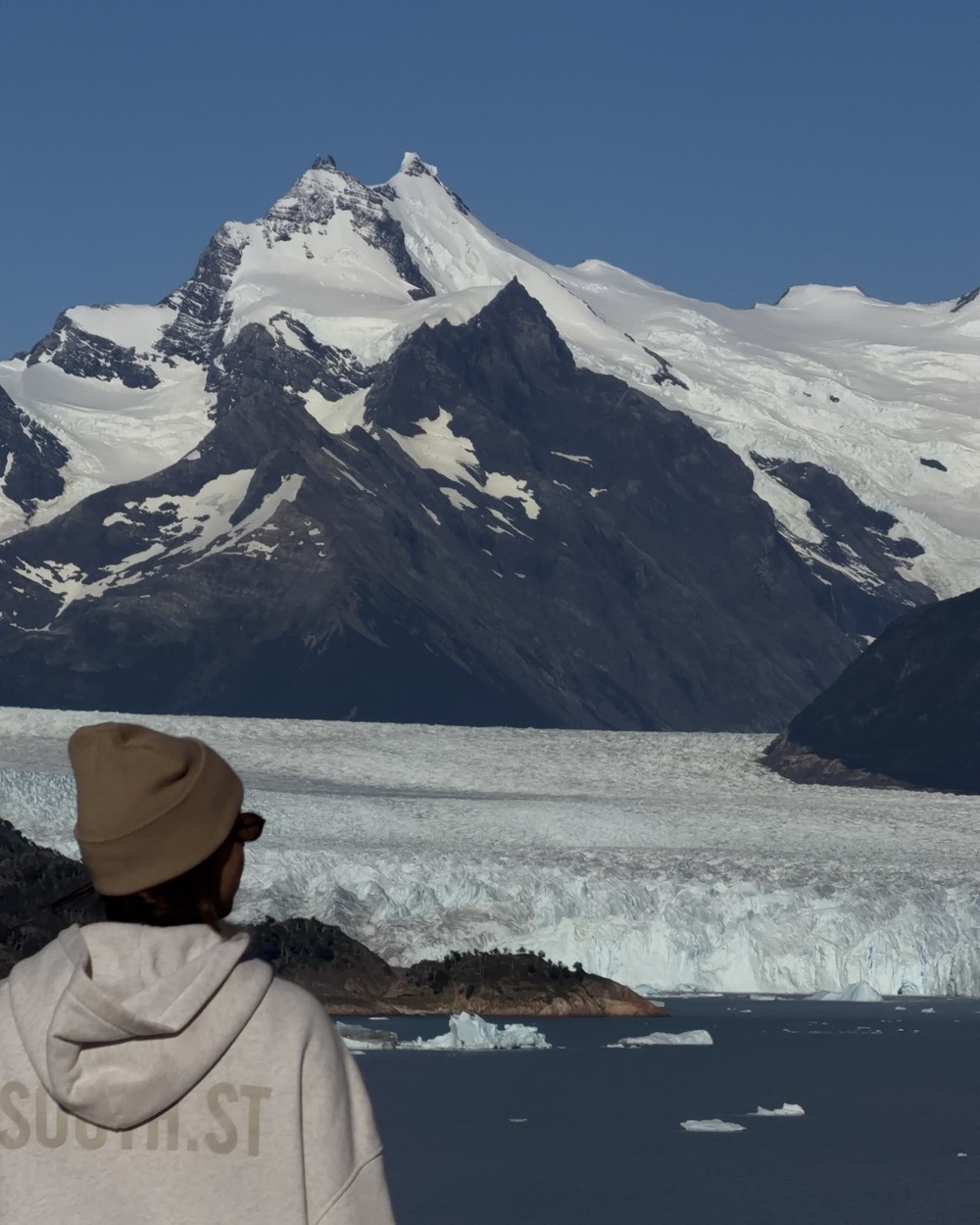 Ellen in a beanie looking out at Perito Moreno Glacier and snowy peaks under a cloudless blue sky