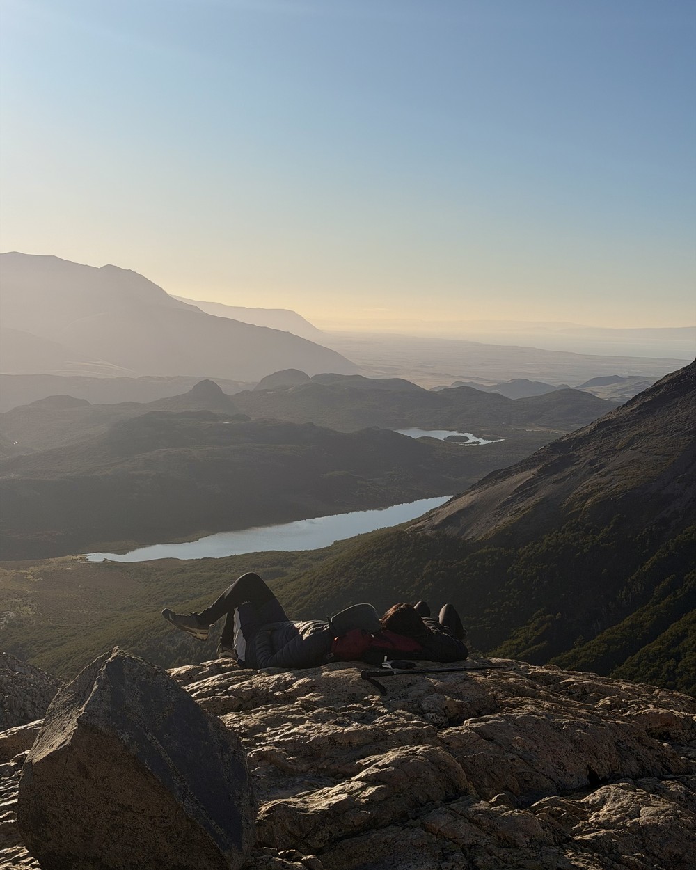 Hikers resting on a rock in early morning light, with lakes in the valley below the Fitz Roy trail