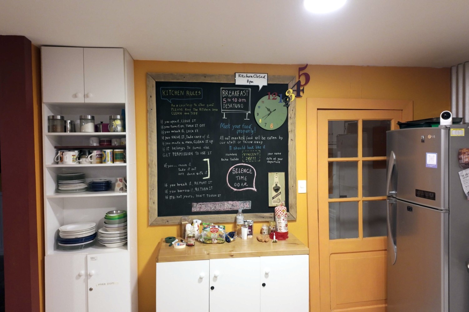 The shared kitchen at El Patagónico Hostel, with a chalkboard of kitchen rules, shelves of plates and a fridge