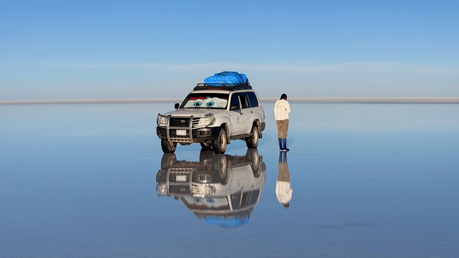Ellen beside our four-wheel drive reflected on Bolivia's Uyuni salt flats at sunrise