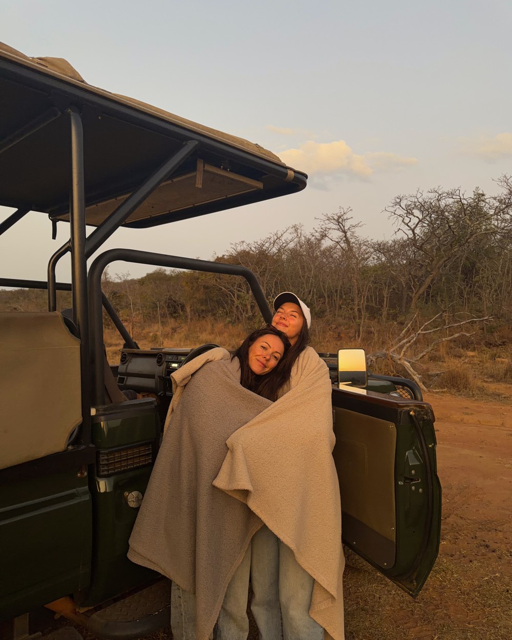 Two people huddled together against the cold on a morning game drive