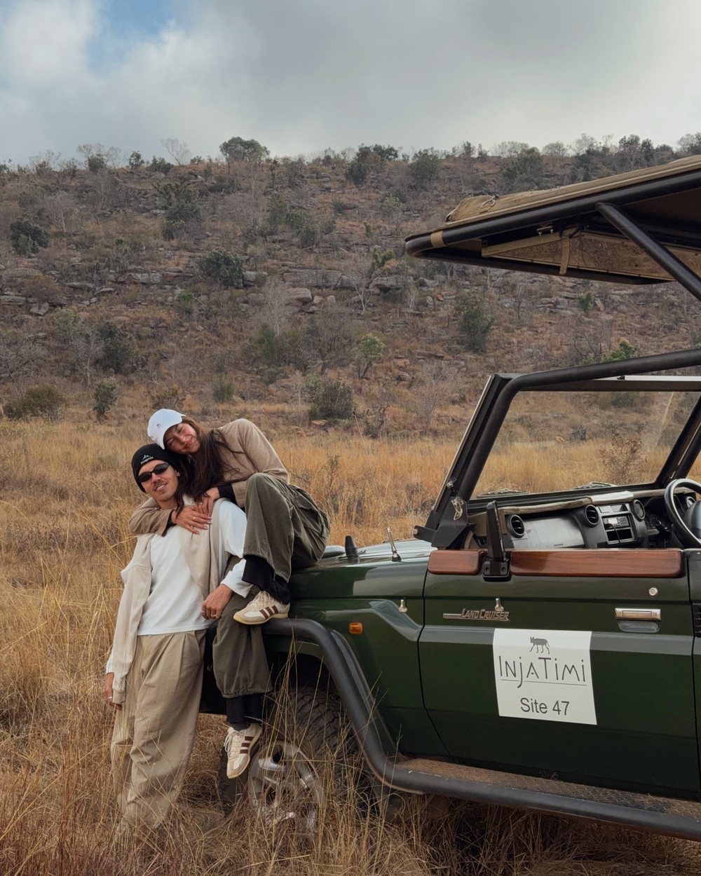 Couple standing beside an open safari vehicle in dry winter grassland