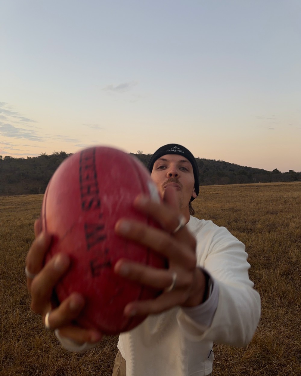 Man holding an Australian football in open grassland at a safari lodge