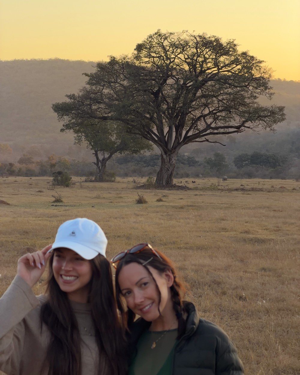 Two people standing in golden grassland at sunrise with a tree behind them