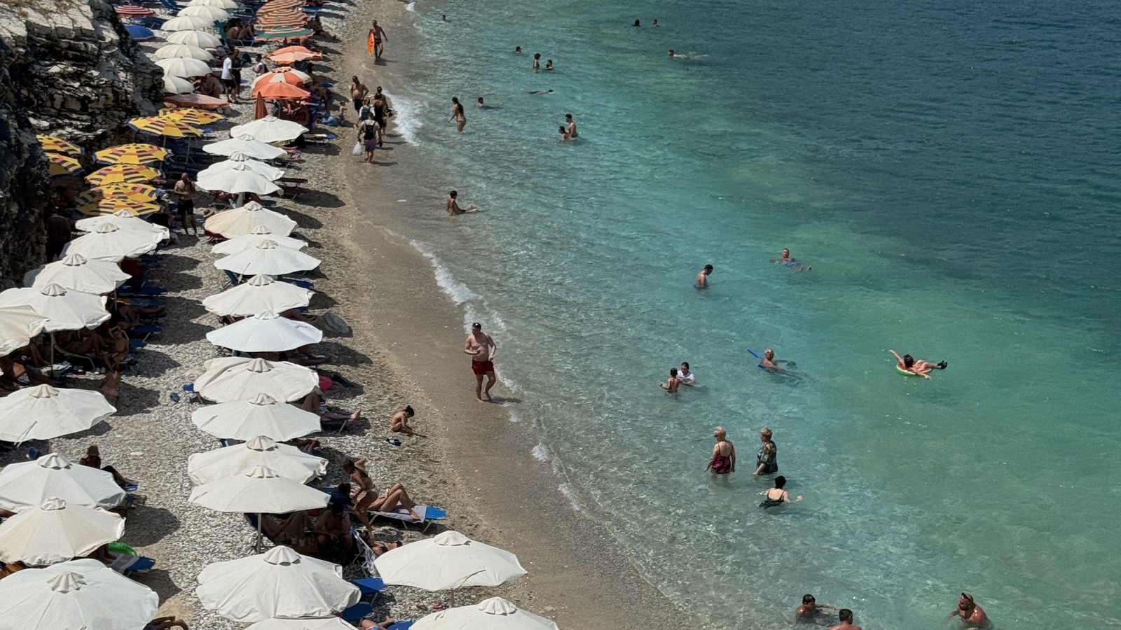 Beach umbrellas lining the shore beside turquoise water at Ksamil, Albania